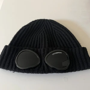 Svart CP Company mössa - Snygg svart ribbad mössa från C.P. Company. Välskött, köpt från NK med tags och certifikat. Skriv vid