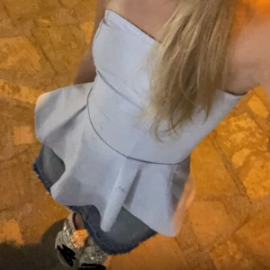 Ljusblå axelbandslös topp - Snygg ljusblå axelbandslös topp med en peplum-design som ger en elegant siluett. Perfekt för att klä upp sig lite extra. Toppen har en figurnära passform och är tillverkad i ett mjukt material. 