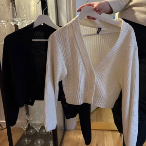 Vit och svart stickad kofta med knappar - Säljer en vit och en svart stickad kofta med v-ringning och knappar framtill. Koftorna har ett ribbat mönster