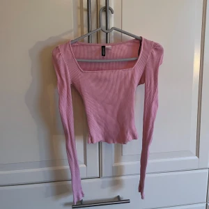Rosa ribbad topp från H&M - Säljer en söt rosa ribbad topp från H&M. Toppen har en fyrkantig halsringning och långa ärmar, perfekt för en stilren look. Den är både bekväm och trendig, idealisk för olika tillfällen.