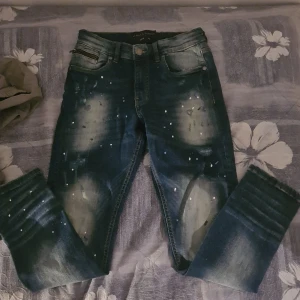 Mörkblå jeans med slitningar från Supply & Demand - Snygga mörkblå jeans från Supply & Demand med coola slitningar och blekta detaljer. De har en klassisk femficksdesign och knappgylf. Perfekta för en avslappnad stil med en touch av edge.