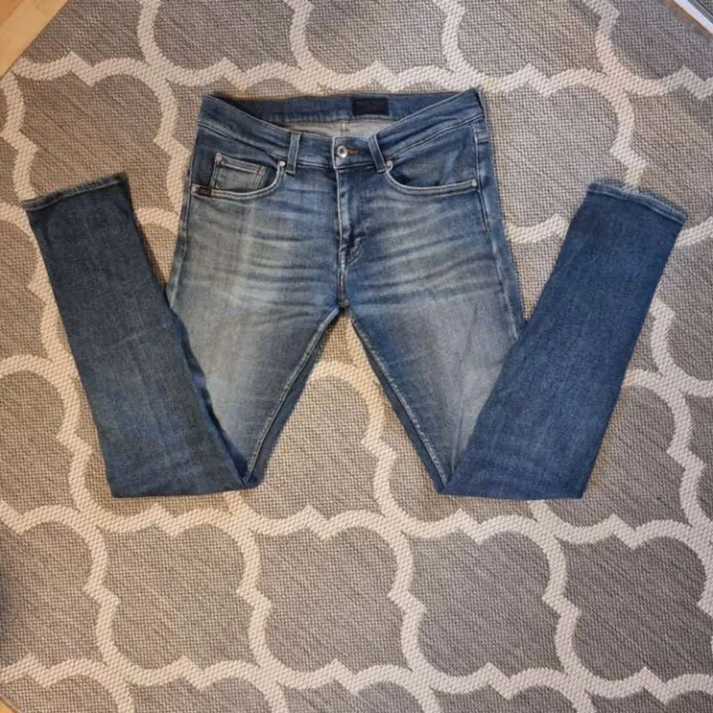 Snygga blå jeans med en klassisk femficksdesign och slitningar för en trendig look. De har en knappgylf och bälteshällor. Perfekta för en avslappnad stil.. Farkut & Housut.