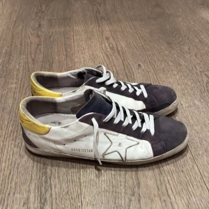 Golden Goose sneakers med stjärndetalj - Snygga sneakers från Golden Goose i vitt och blått med gul häl och stjärndetalj på sidan. Skorna har snörning och en unik design med en sliten look. Perfekta för en avslappnad stil.