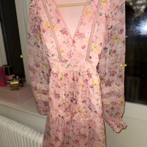 Rosa blommig klänning från Vila❤️ - Söt rosa klänning från Vila med blommigt mönster och spetsdetaljer. Den har en v-ringad hals och långa ärmar med volang och är en kort modell. Perfekt för vår och sommar! Är helt ny och inte använd så inga defekter! Skriv om det finns några funderingar och priset går alltid att diskuteras❤️❤️(Har satt ett spänne i midjan bara för bildens skull på klänningen)