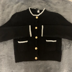 Svart kofta från H&M med guldknappar - Säljer min svarta kofta från H&M med dekorativa guldknappar och vita kantdetalj då den inte kommer till användning.