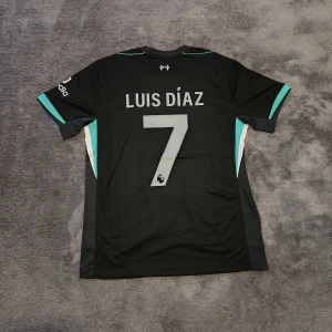 Liverpool FC | 24/25 | Size: L | Bortatröja | Luis Díaz | Ny - Liverpools bortatröja för nuvarande säsong 2024-2025. Luis Díaz, nr 7 på ryggen. Stadium/fan edition. Endast hängt på galge så helt ny & oanvänd. Storlek large. Tröjan är en nyproducerad reprint i utmärkt kvalitet. Perfekt för alla Liverpool fans där ute!⚽  Skickas 1-3 dagar efter mottagen betalning. Har du frågor/funderingar är det bara att höra av dig! :)