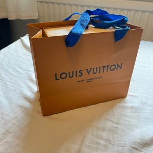 Louis Vuitton Bälte - Säljer ett svart bälte från Louis Vuitton med ikoniskt LV-spänne i svart metall. Bältet har diskret rutmönster och levereras i original ask, dustbag och påse med blå detaljer. Perfekt accessoar för att lyfta vilken outfit som helst. Använd fåtal gånger. Märks inte att den är använd. 110 cm. Köpt från Stockx