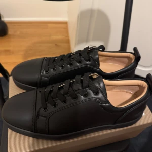 Svarta sneakers från Christian Louboutin(Pris kan diskuteras) - Snygga svarta sneakers från Christian Louboutin i skinn med klassisk röd sula och svarta skosnören. Stilren design med rund tå och diskreta detaljer, perfekt för dig som gillar exklusiva och trendiga skor.