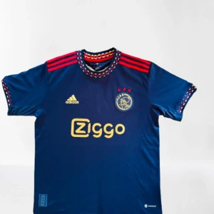 Ajax amsterdam limited edition - Visa ditt stöd med stil! Denna exklusiva Ajax Amsterdam matchtröja i mörkblå design med röda detaljer är ett måste för varje äkta fotbollsfantast. Med ikoniska Ziggo-sponsorn, Adidas-loggan och Ajax-emblemet med tre stjärnor, kombinerar den här tröjan klassisk stolthet med modern design.  ✨ Funktioner:  	•	Elegant mörkblå färg med röda ränder och detaljer 	•	Mjuk och bekväm passform – perfekt för både match och vardag 	•	Unisex-modell – passar både herr och Dam 
