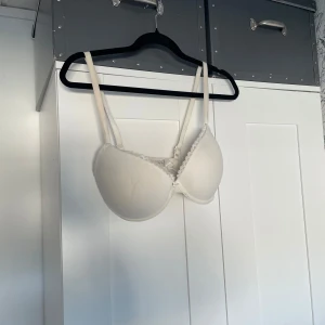 Vit vadderad bh med spetskant 65F - Säljer en vit bh i storlek 65F med vadderade kupor och söt spetskant upptill. Justerbara axelband och klassisk hyskknäppning bak. Perfekt för dig som vill ha en enkel men ändå fin bh under kläderna.