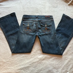 Blå bootcut jeans Underground Soul - Snygga blå bootcut jeans från Underground Soul med broderade bakfickor och klassiska detaljer. Jeansen har låg midja, fem fickor och coola slitningar framtill