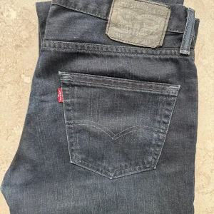 Levi's 511 mörkblå jeans 31/32 - Snygga Levi's 511 jeans i mörkblå tvätt med klassisk femficksdesign och rakt snitt. Jeansen har en diskret snygg slitning. Tillverkade i mjukt och slitstarkt bomullsjeansmaterial. Låg midja, bra skick. 78cm i längd insida ben. 