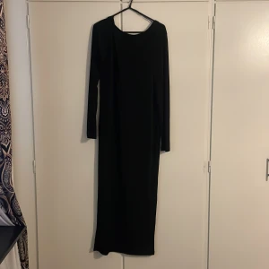 Svart långklänning Black Label - En stilren svart långklänning från The Black Label Collection. Klänningen har lång ärm och rak passform med backless uringad. Perfekt för dig som gillar en minimalistisk och elegant look.