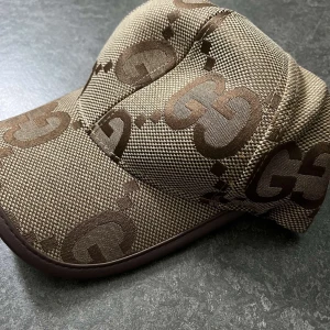 Jumbo GG keps - Snygg beige keps  ikoniskt GG-mönster i brunt. Kepsen är tillverkad i bomull och polyester, har justerbar rem bak i läder och klassisk böjd skärm. Perfekt för dig som vill sticka ut med en lyxig accessoar.