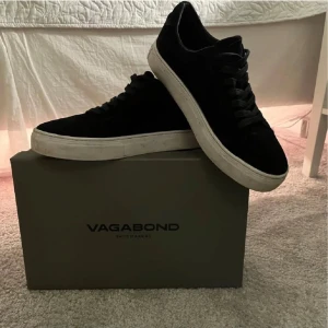 Svarta sneakers från Vagabond, strl 40 - Snygga svarta sneakers från Vagabond med klassisk låg profil och vit platt sula. Skorna har rund tå, snörning och är tillverkade i mocka för en stilren och trendig look. Perfekta för dig som gillar minimalistisk stil och vill ha ett par bekväma vardagssneakers. Låda och kvitto finns