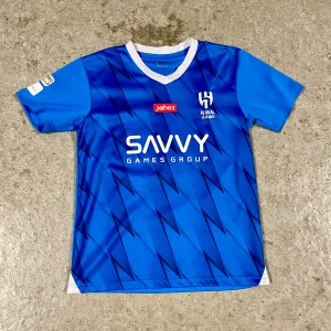 Al-Hilal Neymar Jr #10 – Matchtröja (Replika) ( Barn) - Säljer en blå Al-Hilal-replika med Neymar Jr #10, baserad på säsongen 23/24 då han gick till klubben. Ej officiell, men snygg och välgjord med tryckta sponsorer och namn. Storlek 152 (12 år), normal passform. 100 % polyester, snabbtorkande och lätt. Knappt använd, i mycket fint skick. Tvättad och redo att bäras. Perfekt för dig som vill bära Neymars tröja utan att betala dyrt. Skickas snabbt! Hör av dig vid frågor eller om du vill se fler bilder.