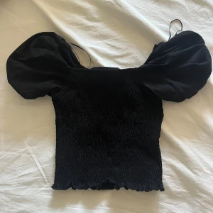 Svart puffärm topp med smock - Supersnygg svart topp med smockad kropp och stora puffärmar från Gina tricot. Toppen är croppad och har en fyrkantig halsringning. I princip oanvänd då det inte riktigt är min stil💕