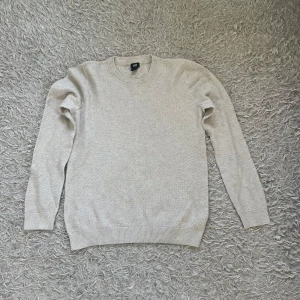 Beige stickad tröja från H&M - Snygg beige stickad tröja från H&M i storlek M. Tröjan har rund halsringning, ribbade muddar och är långärmad. Perfekt för lager-på-lager och passar till både jeans och chinos. Enkel och stilren design som funkar året runt.