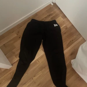 Svarta mjukisbyxor med patch - Svarta mjukisbyxor med en liten vit patch på höften. Byxorna har en avslappnad passform och är perfekta för chill dagar hemma eller när du vill vara bekväm. Klassisk look som funkar till det mesta.