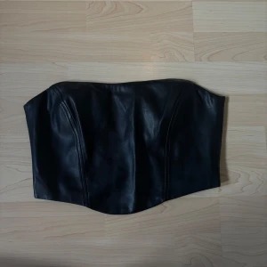 Svart skinntopp från Nelly stl 36 - Svart topp från Nelly i skinnimitation. stl 36. Använd 1 gång. Fint skick, inget att anmärka på!  Dragkedja i bak.