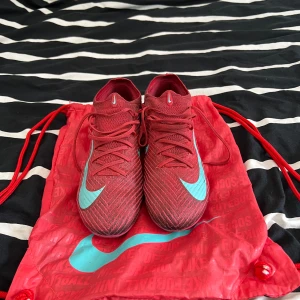 Nike röda fotbollsskor Gripknit - Snygga röda Nike fotbollsskor med turkosa detaljer och Nike Gripknit-överdel. Skorna har snörning, stickad ovandel och en cool sula i rosa och turkos med Air Zoom-teknologi. Perfekta för dig som vill sticka ut på planen och ha grym känsla på bollen. PRIS KAN DISKUTERAS 