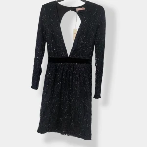 Svart glittrig kortklänning med öppen rygg NLY - Supersnygg svart kortklänning från Nly by Eve  med glittriga paljetter, djup v-ringning och öppen rygg. Klänningen har lång ärm, sammetsband i midjan och knappar i nacken. Perfekt för dig som vill sticka ut med en elegant och trendig look.