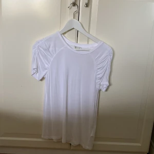 Vit t-shirt med rynkade ärmar  - Vit t-shirt från C i mjukt material med korta ärmar och snygga rynkade detaljer vid axlarna. Enkel och stilren modell med rund halsringning, perfekt för en clean look. jätte stretchig.