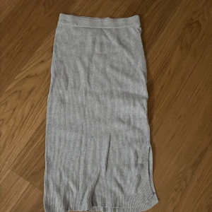 Ljusgrå ribbad långkjol Gina Tricot - Säljer en ljusgrå ribbad långkjol från Gina Tricot. Kjolen har en rak passform, mjukt stretchigt material och en snygg slits på sidan. Perfekt för dig som gillar enkel och stilren look. Storlek L men passar även M 