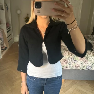Svart lurvig kofta - Säljer en svart, croppad cardigan jacka med trekvartsärm och mjuk, fluffig känsla. Jackan har en klassisk krage och knäppning framtill. Perfekt för dig som gillar en enkel men ändå trendig look. Passar snyggt över linne eller t-shirt. Från saint tropez
