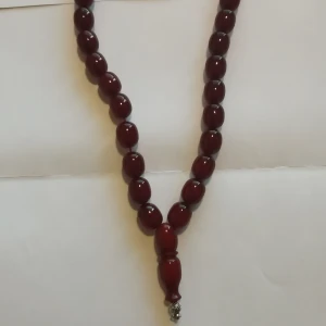 Mörkröd Tasbih pärlhalsband med silverdetalj - Snygg Tasbih halsband med stora, ovala pärlor i mörkröd färg och en dekorativ silverfärgad detalj längst ner. Perfekt accessoar för att lyfta din outfit med en elegant touch och unik design.