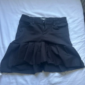 Svart jeanskjol med volangkant - Svart kort jeanskjol med råa kanter och bred volang nedtill. Kjolen har klassiska jeansfickor fram och bak, bälteshällor och dragkedja framtill. Snygg och edgy stil som passar perfekt till sneakers eller boots. Omgjord av ett par gamla jeans från Lindex, har sytt själv. Om man inte är nöjd med sidorna går de att klippa och ändras på, med hjälp av symaskin!