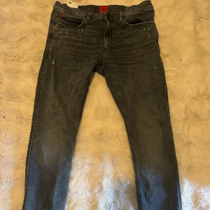 Mörkgrå skinny jeans från Hugo - Snygga mörkgrå jeans från Hugo med skinny passform. Jeansen har klassisk femficksdesign, diskreta slitningar framtill och röd Hugo-label bak i midjan. Tillverkade i stretchig denim för en bekväm känsla och tight look.
