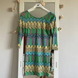 Färgglad kortklänning från Topshop - Snygg kortklänning från Topshop med färgstarkt grafiskt mönster i grönt, gult, blått och rosa. Klänningen har trekvartsärm, rund halsringning fram och djupare rygg. Tillverkad i mjukt stretchigt material som sitter tight och markerar figuren.