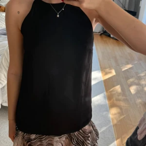 Svart topp  - Enkel och stilren svart ärmlös topp från H&M med hög halsringning. Toppen har en rak passform och är tillverkad i ett mjukt, lätt material som känns skönt mot huden. Perfekt att matcha med kjol eller jeans för en clean look.