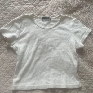 Beige topp från Brandy Melville - Säljer en söt beige topp från Brandy Melville med diskret hålmönster och rund halsringning. Modellen är croppad och har korta ärmar, perfekt till jeans eller kjol. Tunt och mjukt material som känns skönt mot huden.