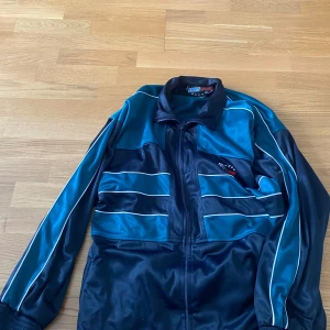 Grön och svart vindjacka från Euro Sport - Säljer en retro vindjacka från Euro Sport i grönt och svart med vita ränder. Jackan har dragkedja framtill, hög krage och långa ärmar med muddar. Perfekt för oversized look. Pris kan diskuteras 