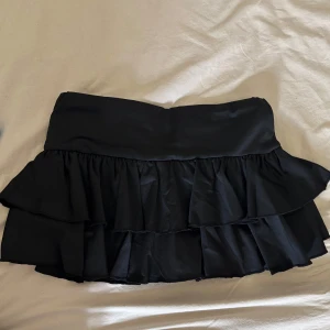 Svart volangkjol i polyester - Supersöt svart kortkjol med dubbla volanger. Kjolen är gjord i ett mjukt polyestertyg som ger ett snyggt fall.