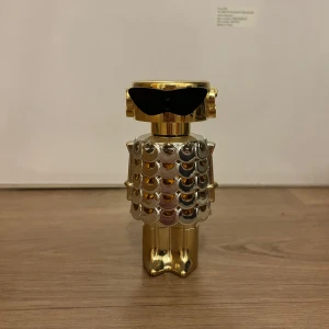 Paco rabanne parfym - Unik parfymflaska från Paco Rabanne i form av en robotliknande figur med guld- och silverfärgad metallfinish och svarta solglasögon. Flaskan har en cool, futuristisk design som verkligen sticker ut i parfymhyllan. Halv full