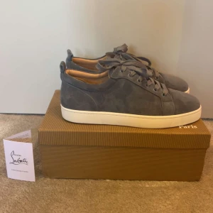 Blå/grå  mockasneakers från Christian Louboutin - Säljer ett par blå/grå sneakers från Christian Louboutin i mocka med klassisk röd sula. Skorna har snörning, vit platt sula och rund tå. Perfekta för dig som gillar stilrena och exklusiva sneakers.