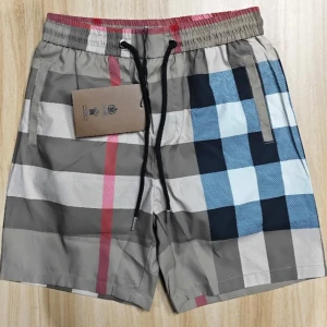 Rutig Burberry badshorts med snörning - Snygga badshorts från Burberry i klassiskt rutigt mönster med beige, blå, svart, vit och röda detaljer. Shortsen har elastisk midja med svart snörning och sidofickor. Perfekta för sommaren och strandhäng.