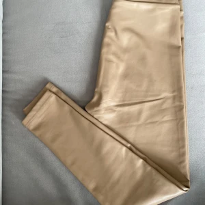 Beige leggings i skinnimitation  - Snygga beige leggings i skinnimitation.  Ger en cool, glansig look. Perfekta att styla med till olika stilar. Fodrade inuti vilket är perfekt till sommarkvällar eller höst. Storleken uppskatas vara en M. 