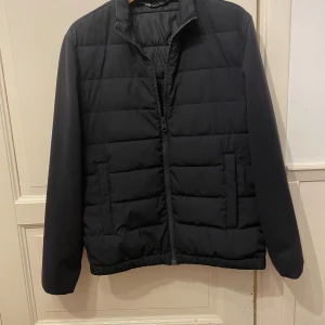 Cardigan  - Snygg mörkblå quiltad jacka från Zara med dragkedja framtill. Jackan har en stilren design med långa ärmar och är perfekt för kyligare dagar. Den har en normal passform och är tillverkad i ett syntetmaterial som håller dig varm.