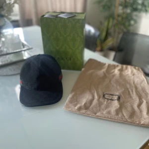Äkta svart Gucci canvas original. Har kvitto för bevis. Kan även ta byten - Snygg svart keps från Gucci med diskret GG-mönster i tyget och klassisk röd-grön rand på sidan. Justerbar rem baktill i metall. Kommer med originalpåse och låda. Den är typ 2-3 månader gammal använd lite men inga märken eller något sånt.