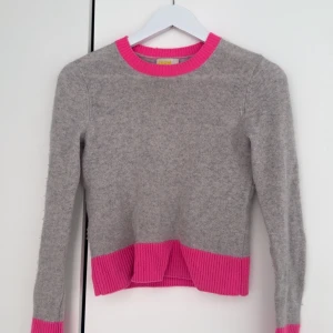 Grå cashmere tröja med rosa detaljer från FROM FUTURE - Supermjuk grå stickad tröja i 100% kashmir från FROM FUTURE. Tröjan har ribbade rosa detaljer vid hals, ärmslut och nederkant samt en croppad passform med snygg slits framtill.  Skulle verkligen säga att tröjan passar storlek XXS-S