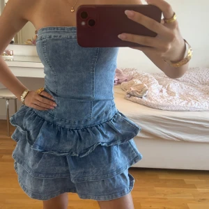 Jeansklänning med volanger - Jättesnygg jeansklänning med volanger😍😍 Klänningen sitter åt i midjan och formar kroppen så snyggt och har även klisterband inuti så den inte trillar av!!! Super bra skick