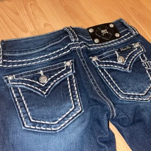 Miss Me jeans med vita sömmar, bootcut - Snygga mörkblå jeans från Miss Me (ny produktion) med tydliga vita kontrastsömmar och dekorativa fickor bak. Bootcut-modell med låg midja. Jeansen är uppklippta till att passa någon runt 150 cm :) Pris kan diskuteras 😛
