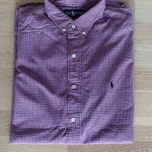Rutig skjorta från Ralph Lauren L - Riktigt snygg rutig skjorta från Ralph Lauren i rött, blått och vitt. Klassisk button-down krage, broderad logga på bröstet och vita knappar. Modellen heter Blaire och är gjord i 100% bomull – perfekt för en clean och stilren look.
