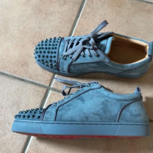Blåa Louboutin sneakers med nitar - Unika blå sneakers från Louboutin i mocka med coola nitar  och klassisk röd sula. Skorna har snörning och en rund tå. Skorna har endast använts 2 gånger OG medföljer såklart.