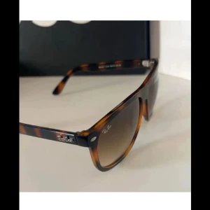 Ray-Ban Wayfarer brunmelerade solglasögon - Snygga Wayfarer solglasögon från Ray-Ban med brunmelerad båge och klassisk form. Glasen är tonade i brunt och bågarna har en cool sköldpaddsmönstrad look. Perfekta för att lyfta din stil under soliga dagar.