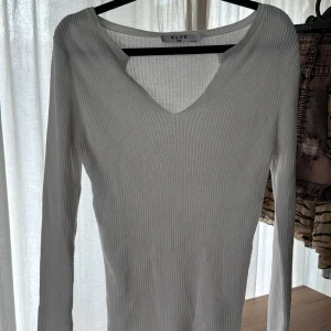 Vit ribbad långärmad topp från NA-KD - Säljer en vit ribbad långärmad topp från NA-KD med v-ringning. Perfekt att styla till jeans eller kjol. Enkel och stilren design som passar till mycket.